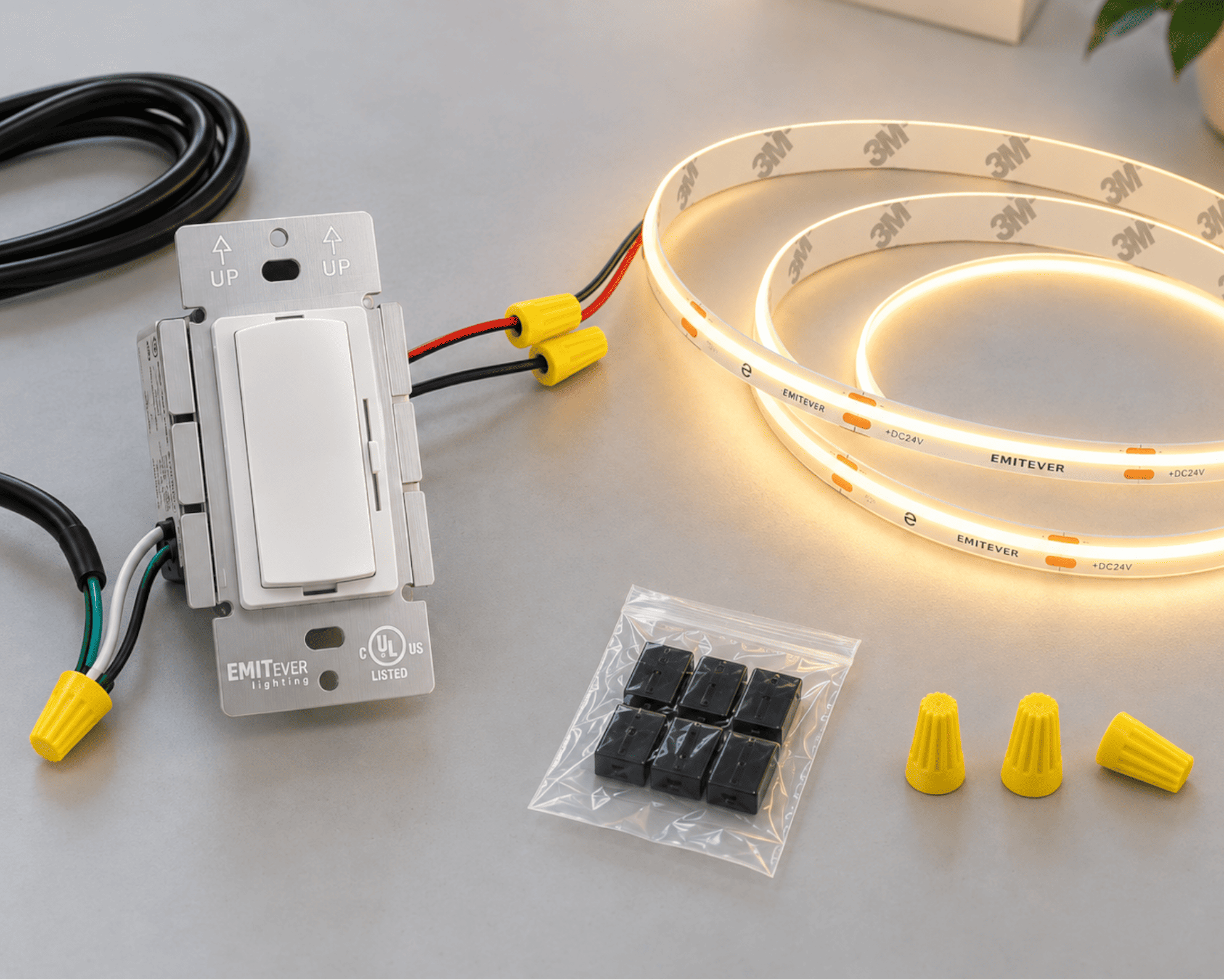 EMITFEVER smart light switch kit with a white single-pole switch, a coiled warm-white LED strip light, yellow wire connectors, black terminal blocks, and yellow wire nuts on a gray surface.